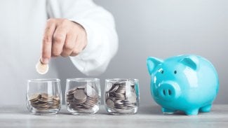 Muž házející mince do keramického prasátka. Koncept úspory peněz, význam vytvoření finančního polštáře pomocí různých metod úspor.